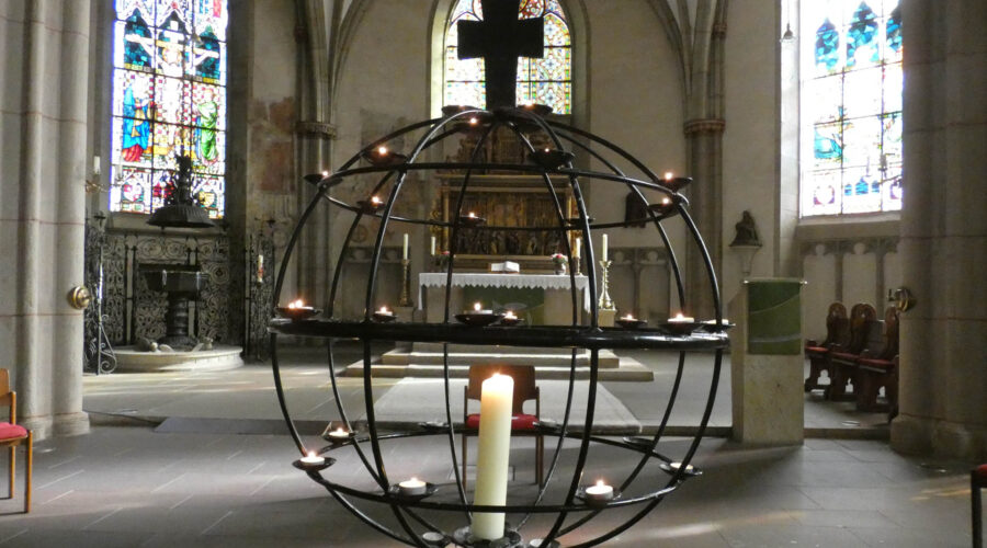 Bild des Altarbereichs der St.-Martini-Kirchengemeinde Stadthagen. Im Vordergrund ein Globus aus Metallstäben, der von einer großen Kerze und vielen Teelichter erleuchtet wird.