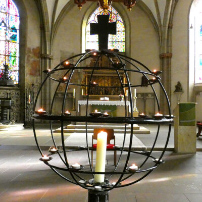 Bild des Altarbereichs der St.-Martini-Kirchengemeinde Stadthagen. Im Vordergrund ein Globus aus Metallstäben, der von einer großen Kerze und vielen Teelichter erleuchtet wird.