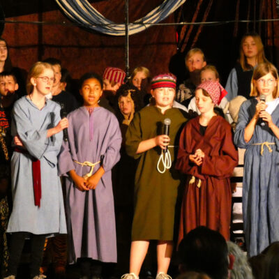 Die Kinder stehen während des Musicals in mehreren Reihen auf der Bühne und singen in ihre Mikrofone.