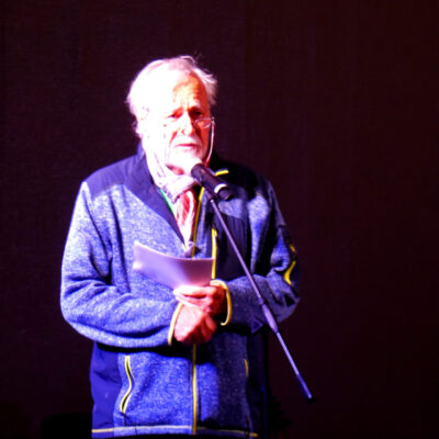 Im Bild steht ein älterer Herr auf der Bühne. Er hält einen Vortrag.